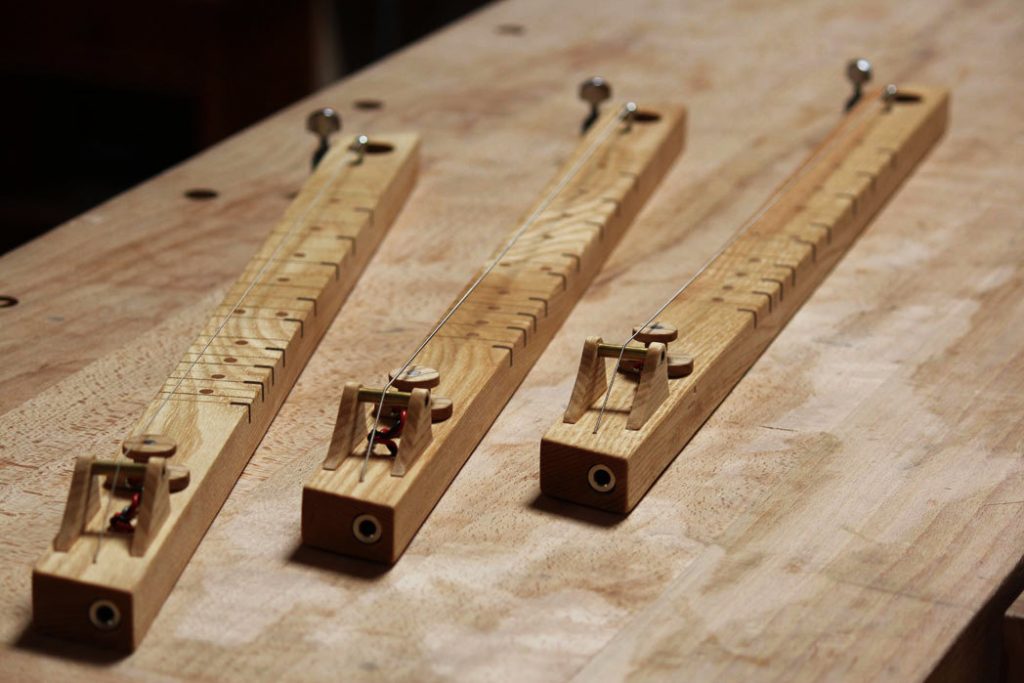 trois pièces de bois avec chacune une corde et un micro magnétique posés sur une table en bois.